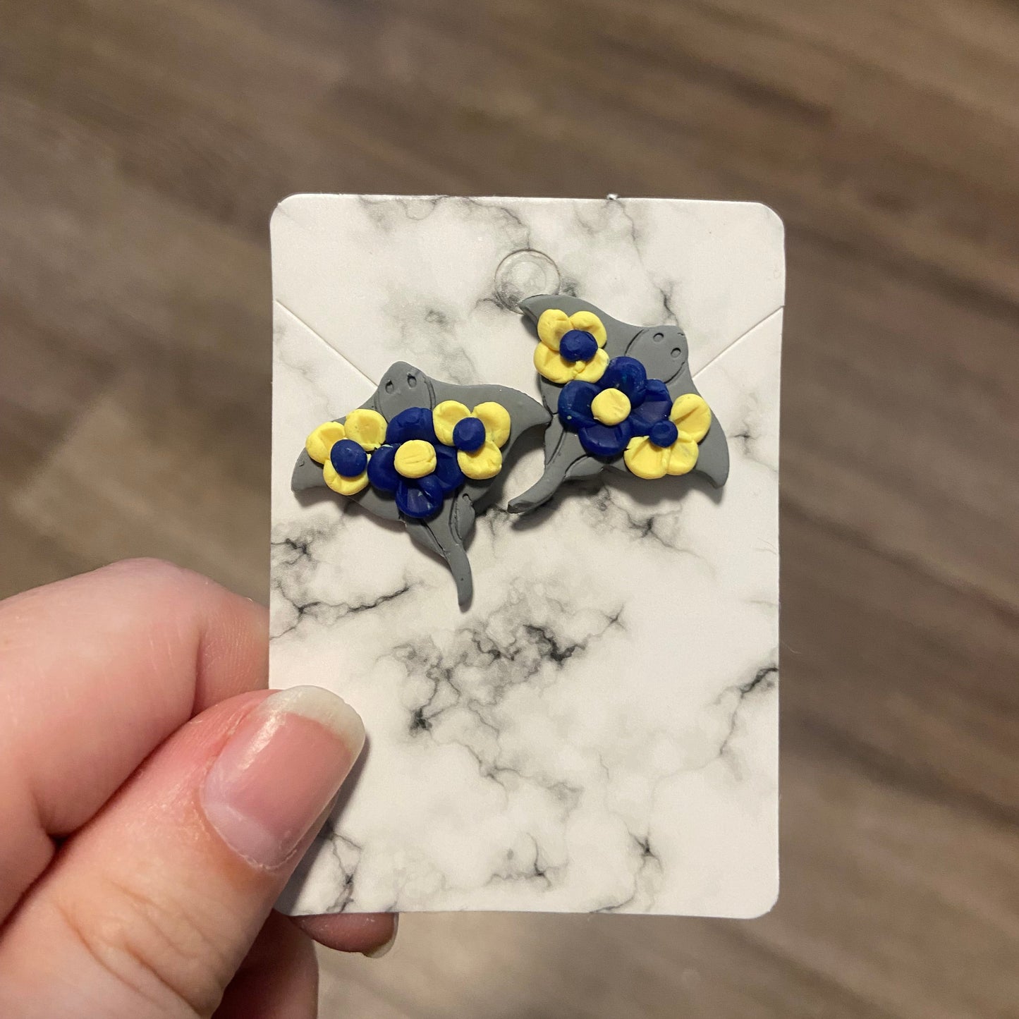 A pair of blue and yellow stingray stud earrings on a white marble pattern card.