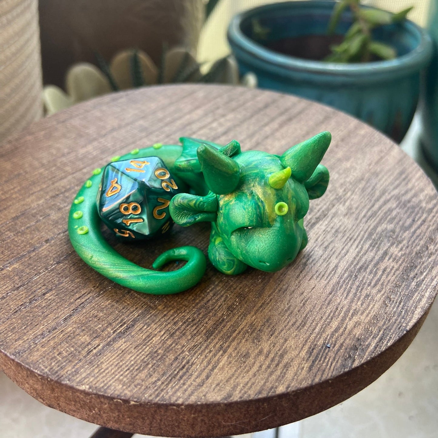 Green dragon figurine with a polyhedral dice on a wooden surface