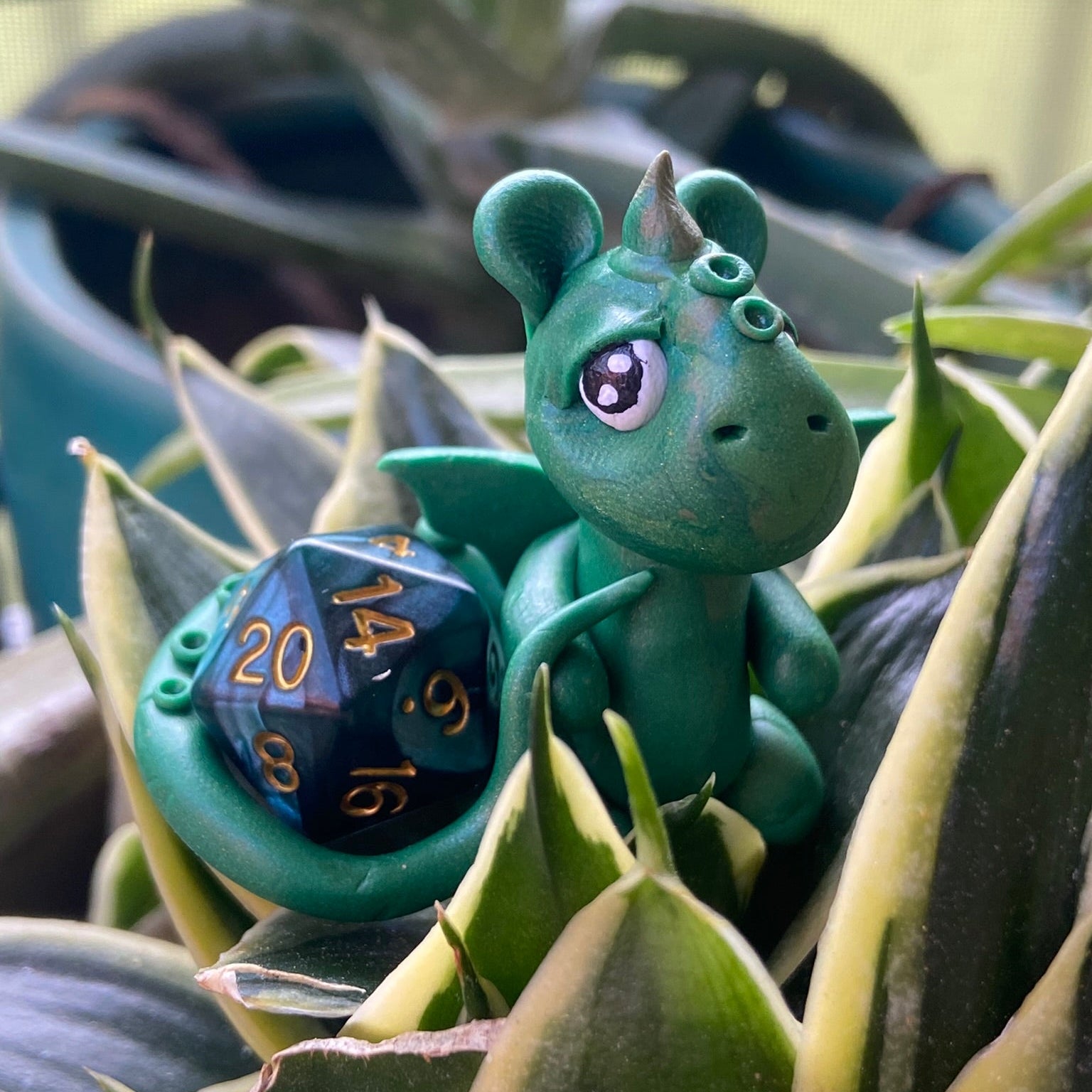 Green dragon figurine holding a blue polyhedral dice among plants